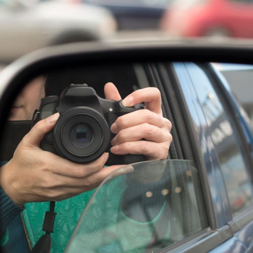 Hidden photographing. Reflection in car mirror of woman with camera.